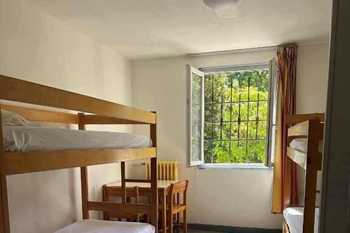 Un dormitorio con literas, un escritorio de madera y una ventana con vistas a vegetación.
