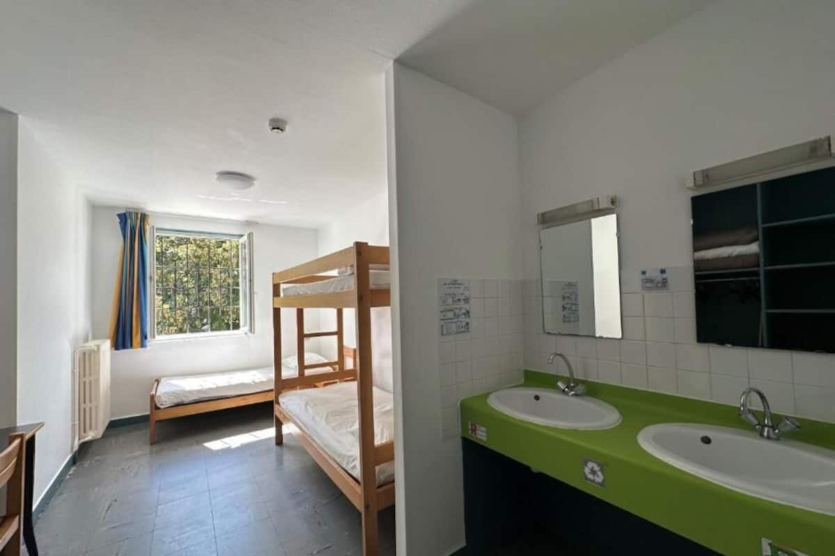 Una habitación con literas, un lavamanos verde y una ventana con cortinas.