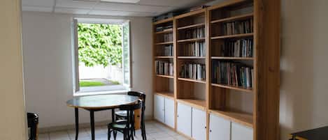 A room with a large bookshelf, a table with chairs, and a window with a view of greenery.