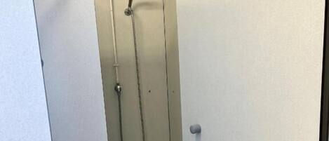Une petite cabine de douche fermée, dotée d’un pommeau de douche à main, de toilettes et d’un lavabo fixé au mur.