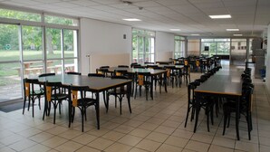 Un amplio comedor interior con varias mesas y sillas, ventanas grandes que dejan entrar luz natural, y vistas al exterior.