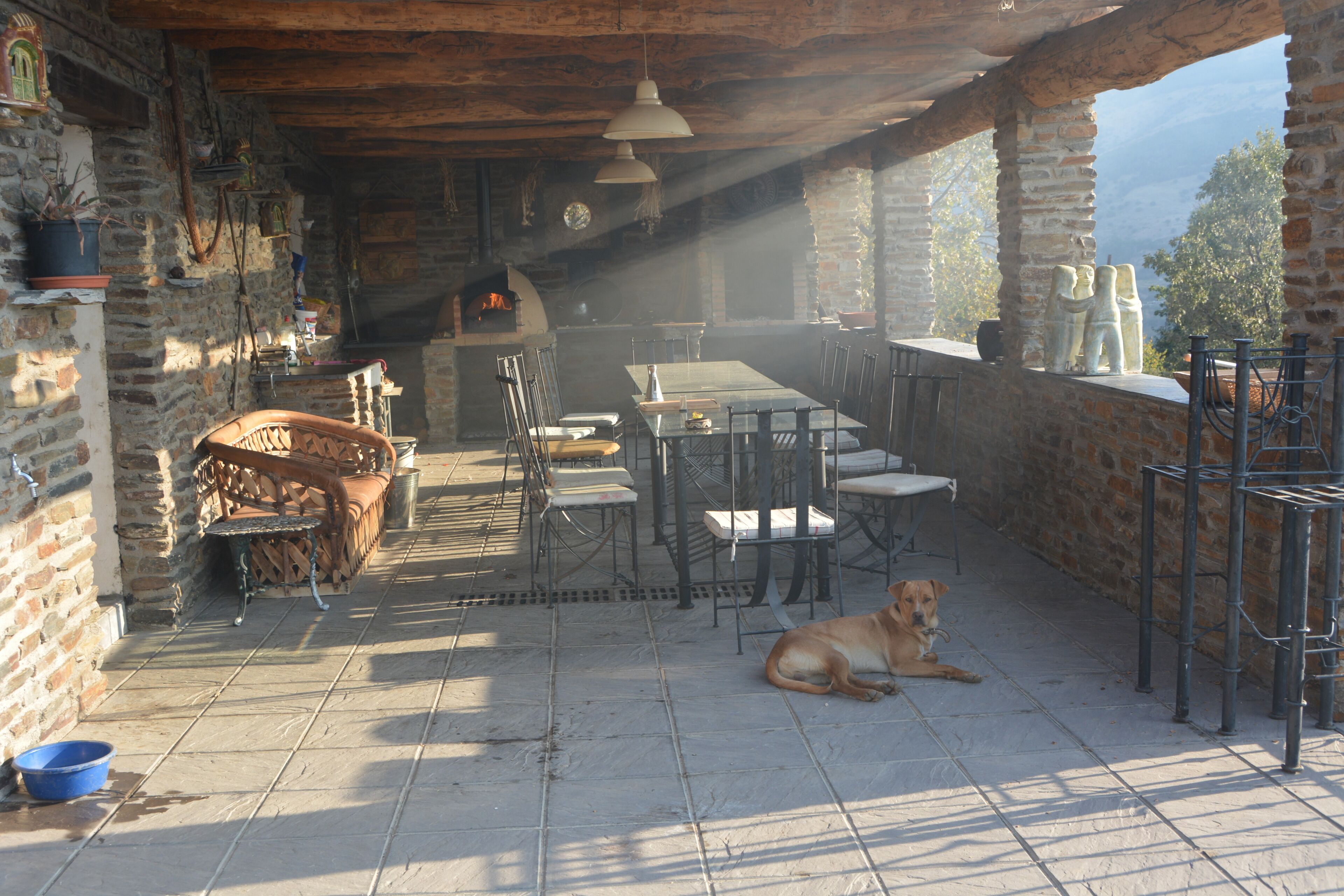 Un espace de restauration extérieur rustique, avec des murs en pierre, une cheminée et un chien qui se repose sur le sol.