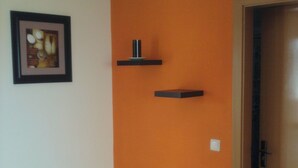 Un couloir avec un mur orange, un tableau encadré et deux étagères noires.