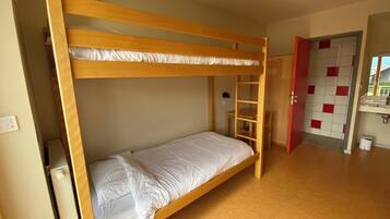 Une chambre avec un lit superposé, une échelle en bois, une petite table et une porte donnant sur une salle de bain carrelée de rouge et de blanc.
