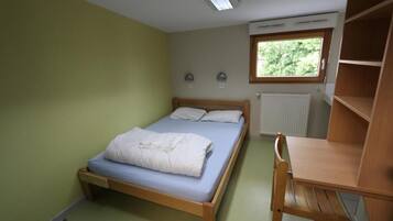 Una habitación pequeña con cama individual, estructura de madera, escritorio y ventana.
