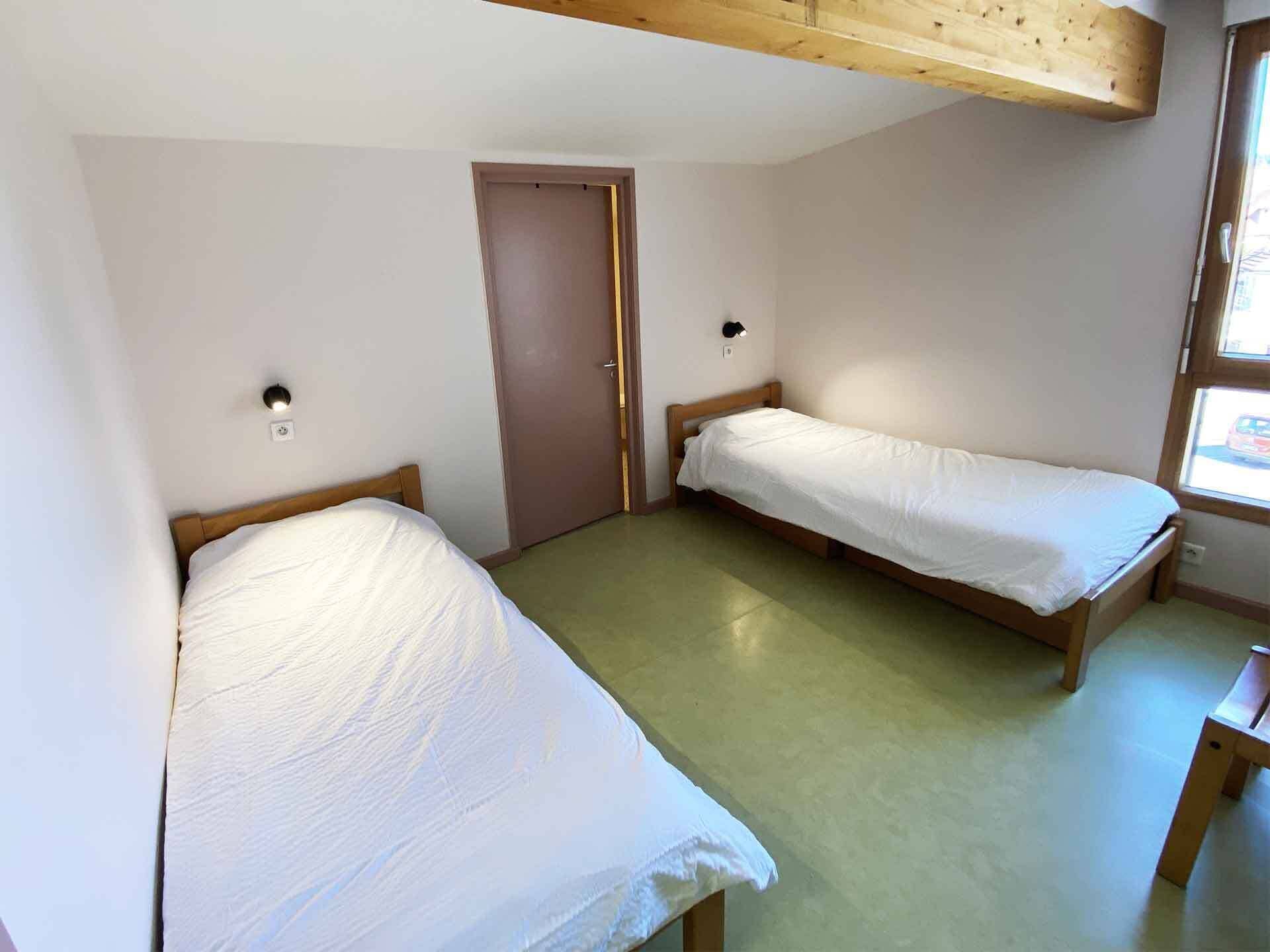 A small, clean room with two single beds, a wooden ceiling, and a window.