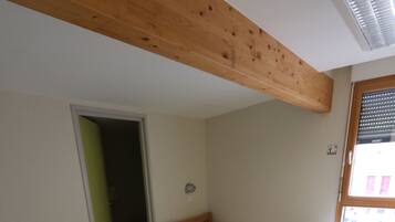 Een kamer met twee houten bedden, een houten tafel en een raam met jaloezieën.