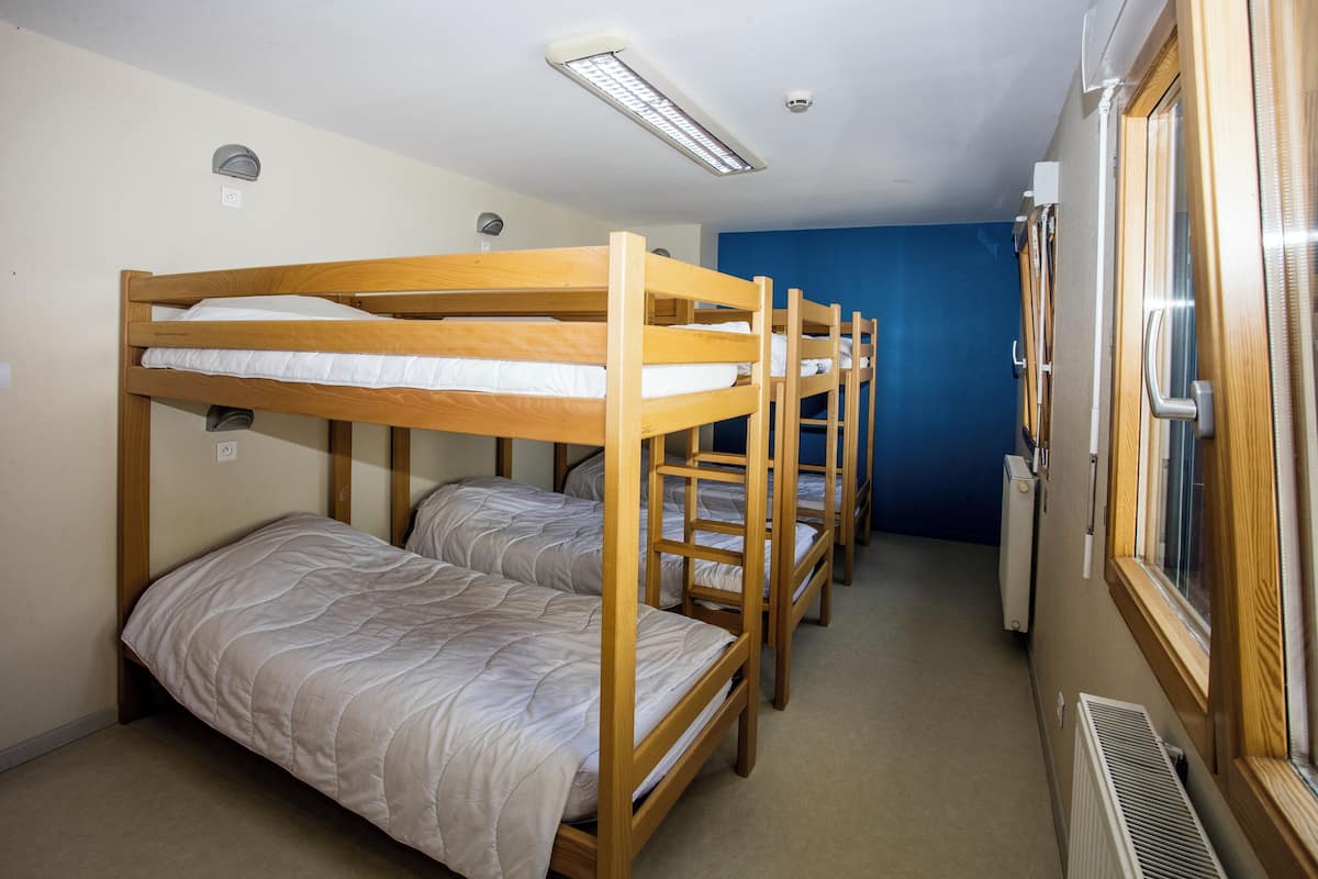 Une chambre de dortoir avec des lits superposés, une fenêtre et un radiateur.