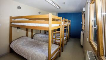 A dormitory room with bunk beds, a window, and a radiator.