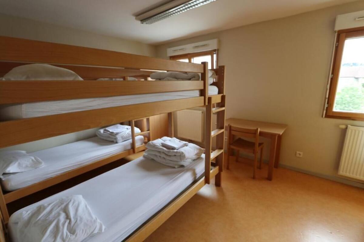 Une chambre avec un lit superposé, un bureau et une chaise, un radiateur et une fenêtre.
