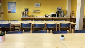 A dining area with wooden tables and chairs, a map on the wall, and kitchen appliances.