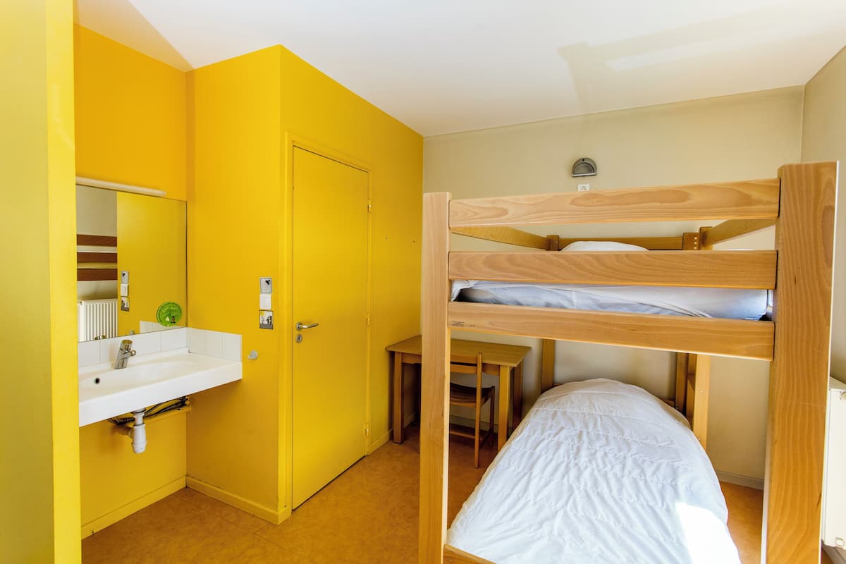 Une petite pièce comprenant un lit superposé, un lavabo et un miroir.
