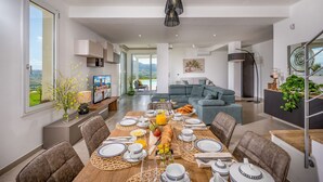 Un comedor moderno con una mesa larga preparada para el desayuno, un sofá al fondo y vistas al exterior.