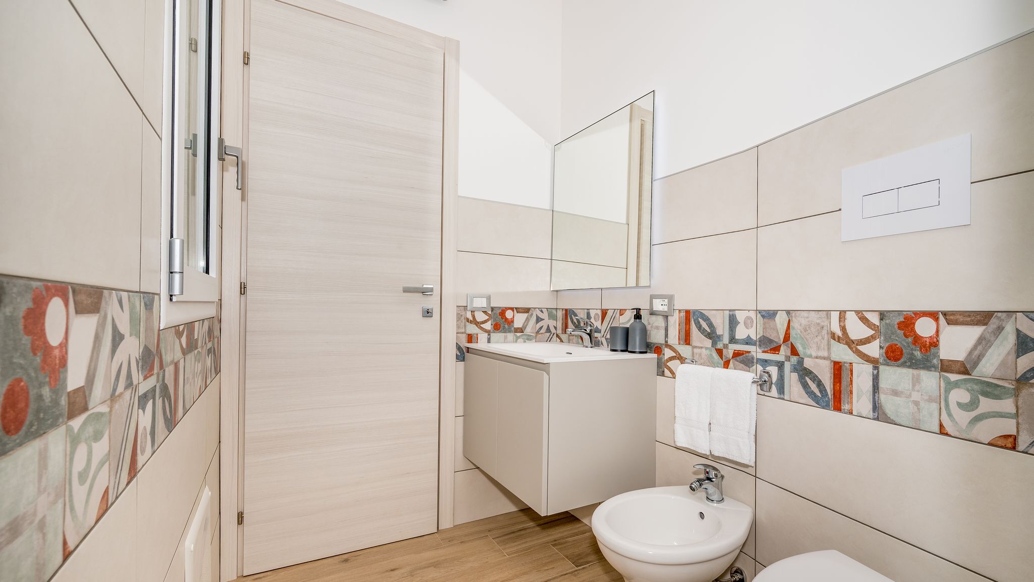 Un baño moderno con puerta de madera, un lavamanos con espejo y un bidé.