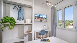 Un dormitorio moderno con cama, escritorio, silla, televisor y vistas al exterior.