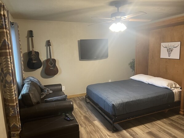 Une chambre à coucher avec un lit, un téléviseur fixé au mur et deux guitares.