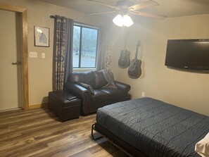 A bedroom with a bed, a couch, a ceiling fan, and two guitars on the wall.