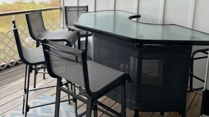A glass-top table with four chairs on a wooden deck, overlooking a body of water. - Mallard Lakes Waterfront Beach Condo in Fenwick Island with Two Pools (Selbyville)