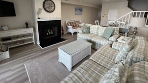 A living room with a fireplace, a sofa set, a television, and a ceiling fan. - Mallard Lakes Waterfront Beach Condo in Fenwick Island with Two Pools (Selbyville)