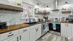Una cocina moderna con armarios blancos, encimera de madera, electrodomésticos de acero inoxidable y un ventanal que proporciona luz natural.