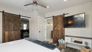 Un dormitorio con cama, televisor, ventilador de techo y una puerta corredera estilo granero.