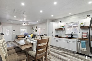 Una cocina moderna con armarios blancos, un refrigerador de acero inoxidable y un comedor con mesa y sillas de madera.
