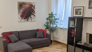 Un salon moderne avec un canapé d’angle gris, une table à manger dressée avec des assiettes et des verres, une bibliothèque et un tableau accroché au mur.