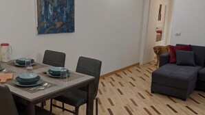 Un coin repas avec une table dressée pour quatre personnes, un tableau accroché au mur et un chien en arrière-plan.