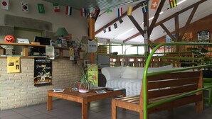 A cozy room with a brick wall, wooden furniture, and a green bench. There are flags hanging from the ceiling and a poster on the wall. - Auberge de Jeunesse HI Pontivy (Pontivy)