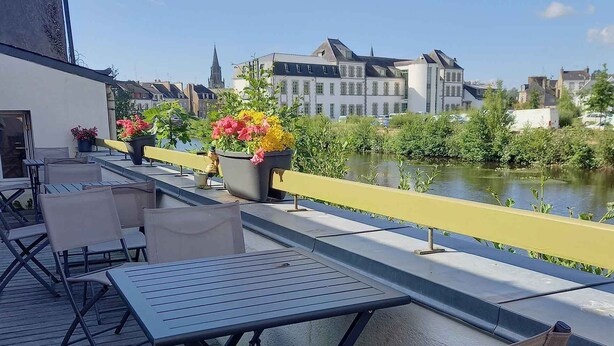 A terrace with outdoor seating, a river view, and buildings in the background. - Auberge de Jeunesse HI Pontivy (Pontivy)