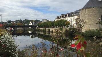 A historic building with a round tower, a bridge, and a calm river reflecting the structure.