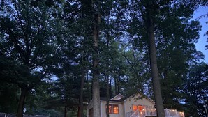 A cabin with a deck and stairs leading to a porch, surrounded by trees. - Charming Lakefront Cottage (Vandalia)