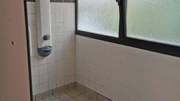 Un baño con paredes de azulejos blancos, un ventanal con vidrio esmerilado y una zona de ducha con desagüe.