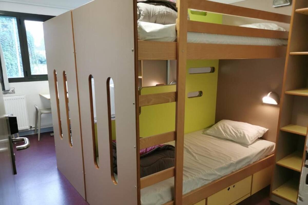 A bunk bed room with a desk and chair, a radiator, and a window.