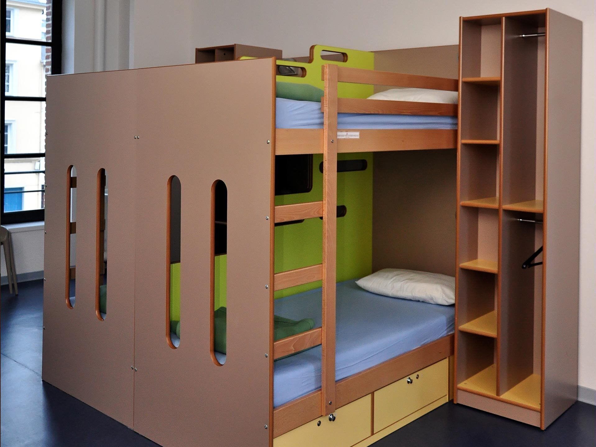 Un lit superposé avec une structure en bois, un compartiment de rangement vert et une armoire intégrée avec des étagères.