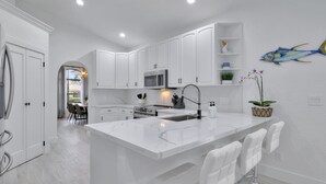 A modern kitchen with white cabinetry, a central island with bar stools, a microwave, and a sink.