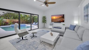 A modern living room with a pool view, a ceiling fan, and a TV on the wall.