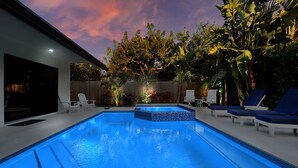 A rectangular swimming pool with a tiled edge, surrounded by lounge chairs and potted plants.