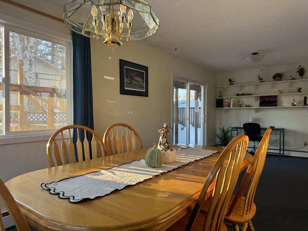 A dining area with a wooden table, chairs, a chandelier, and a view of the outside.