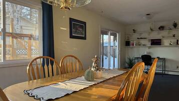 A dining area with a wooden table, chairs, a chandelier, and a view of the outside.
