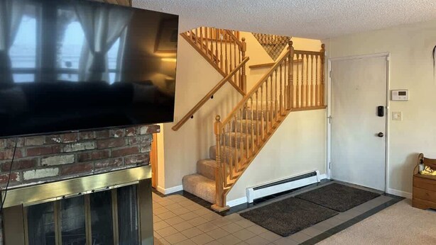 Una sala de estar con chimenea, un televisor montado en la pared, una escalera de madera y una puerta con termostato.