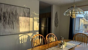 Un comedor con mesa y sillas de madera, una araña y un cuadro abstracto grande en la pared.