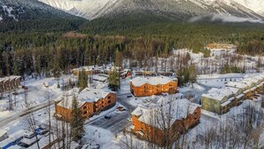 Un complejo turístico nevado con varias edificaciones, una carretera y una montaña boscosa al fondo.