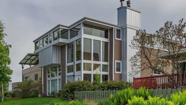 A modern two-story house with large windows, a visible chimney, and a well-maintained garden with various plants and a wooden fence. - 2 Bedroom Modern Condo in Heart of Downtown (Anchorage)