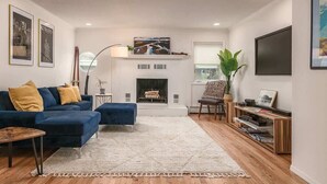 A modern living room with a fireplace, blue sofa, and a bookshelf. - 2 Bedroom Modern Condo in Heart of Downtown (Anchorage)