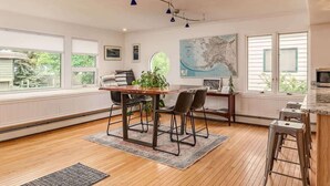 A spacious kitchen with a wooden table, bar stools, and a large window offering a view of the outdoors. - 2 Bedroom Modern Condo in Heart of Downtown (Anchorage)