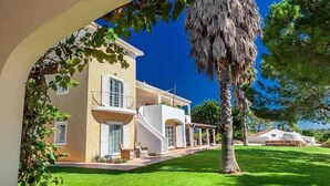 Una casa de dos pisos con balcón, césped cuidado y una palmera.