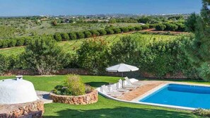 A swimming pool with a stone border, surrounded by a well-maintained lawn and a stone wall.