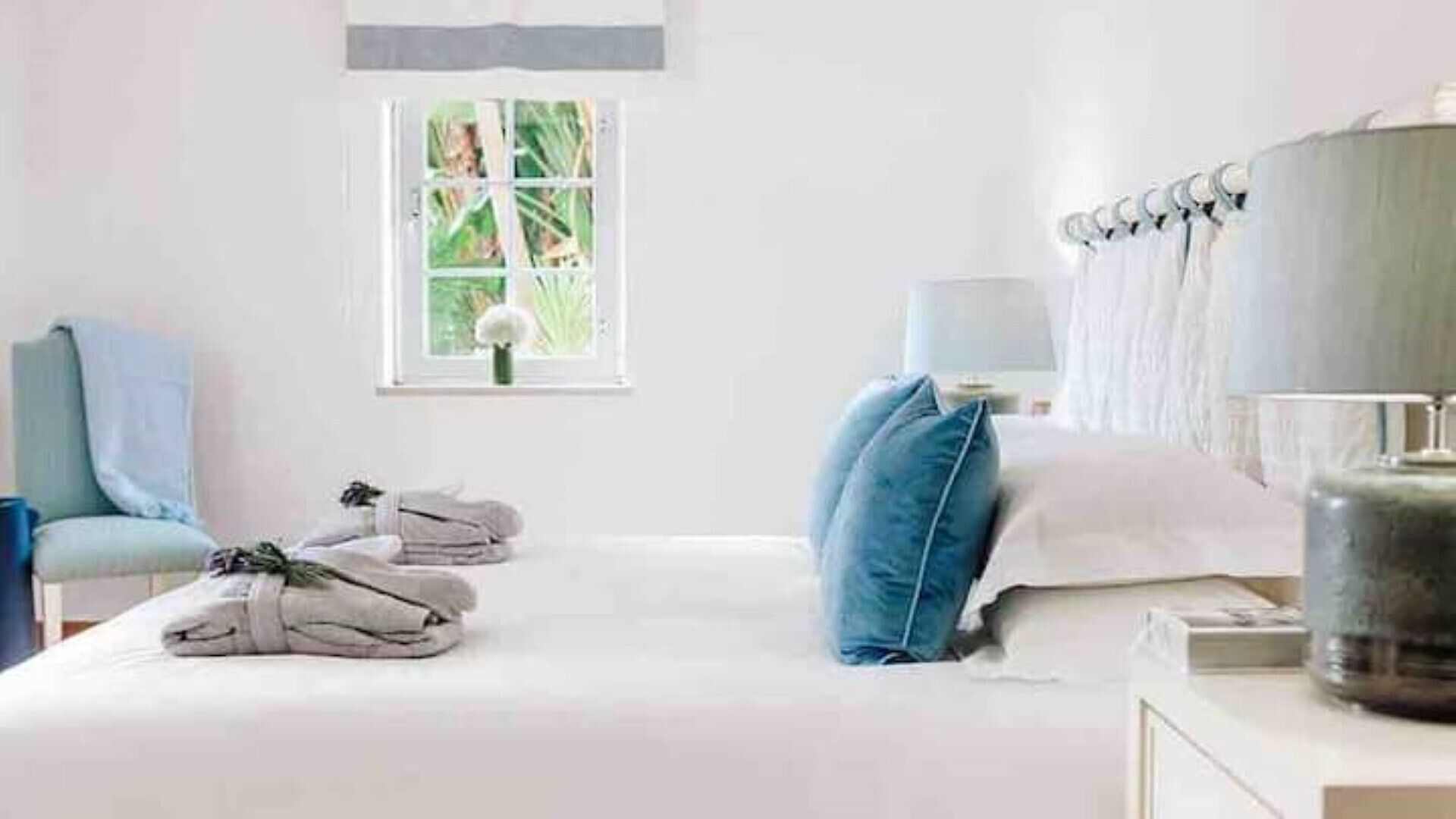 Een hotelkamer met een bed, een stoel, een raam met uitzicht op groen en een lampje op het nachtkastje.