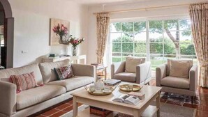 Un salón con sofá, dos sillones, una mesa de centro y un ventanal con cortinas.